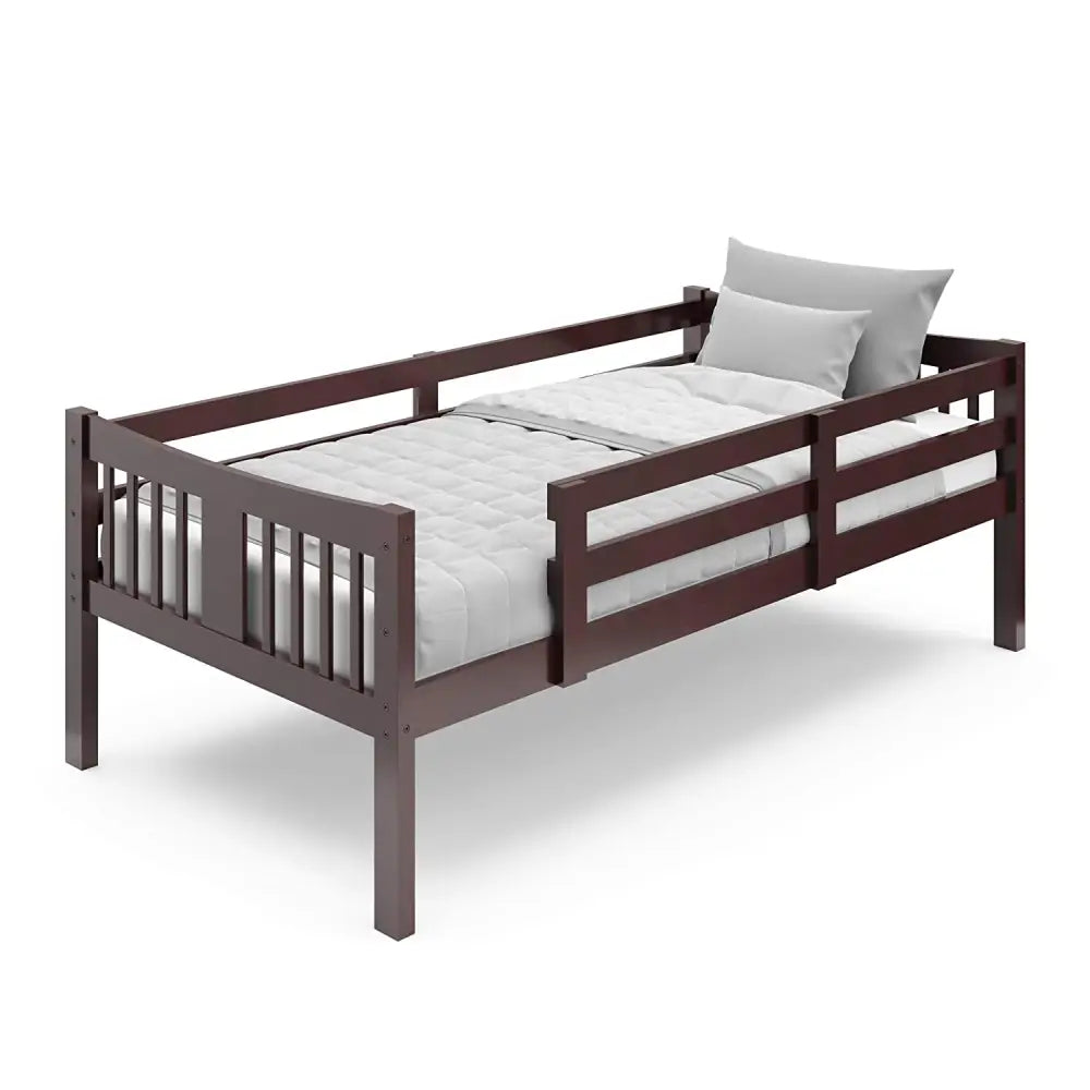 Dark brown wooden toddler bed with slatted design, safety rail, gray mattress, and pillow