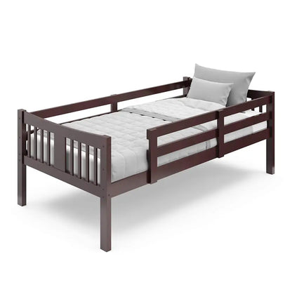 Dark brown wooden toddler bed with slatted design, safety rail, gray mattress, and pillow